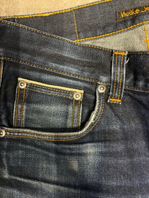 *SELVEDGE* nudie jeans - Snygga mörkblå jeans från Nudie Jeans med klassisk femficksmodell och kontrastsömmar i orange. Jeansen har en go passform och slitningar för en cool, använd look. Tillverkade i denim med tydlig struktur. Modellen är Lean Dean och i storlek 29:30