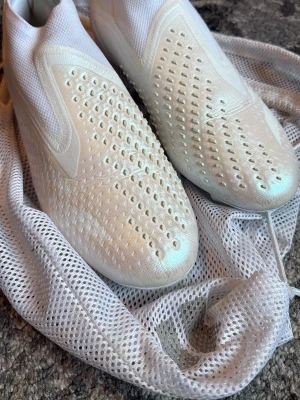 Vita Adidas Predator fotbollsskor - Säljer ett par vita Adidas Predator fotbollsskor utan snörning. Skorna har en strumpliknande passform och gummidetaljer på ovandelen för extra grepp på bollen. Tillverkade i syntetmaterial och mesh för bra ventilation. Perfekta för dig som vill ha kontroll på planen.