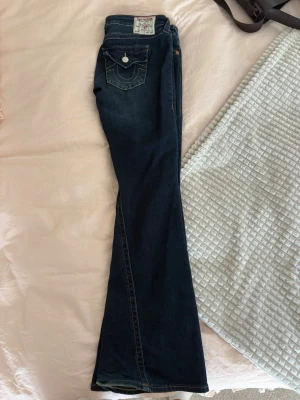 Mörkblå lågmidjade true religion jeans - Super snygga mörkblå true religion jeans, perfekta nu till hösten!🤎 Det är lågmidjade flares. Dem är lite slitna vi nedre delen baksida byxben, se sista bilden. Annars är de i utmärkt skick och behöver tyvärr sälja dem då de inte passar mig i storleken längre.
