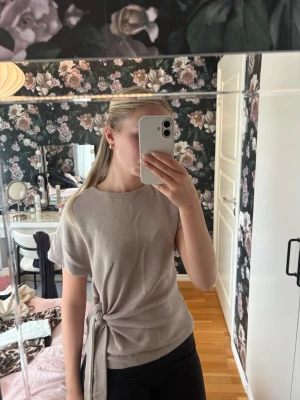 Beige topp med knyt från Zara - Säljer en beige topp från Zara med korta ärmar och rund hals. Toppen har en snygg knyt-detalj i sidan som ger en cool och modern look🌸