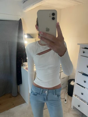 Vit ribbad topp med cut out-detalj - Trendig vit ribbad topp med lång ärm och unik cut out-detalj vid halsen från Gina tricot. Toppen är figurnära och har en stilren look som passar perfekt till jeans eller kjol. Materialet känns mjukt och stretchigt för en bekväm passform.