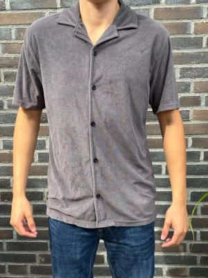 Grå kortärmad skjorta med knappar - Säljer en grå skjorta i mjukt material med korta ärmar och klassisk krage. Skjortan har knappar hela vägen framtill och en avslappnad passform. Perfekt till jeans eller shorts för en chill look. Skriv gärna vid frågor! Modell:180/70kg