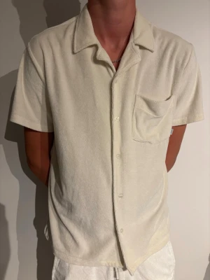 Beige frottéskjorta med kort ärm - Snygg beige skjorta i mjuk frotté med korta ärmar och klassisk krage. Skjortan har bröstficka och knäppning framtill, perfekt för en avslappnad och trendig look.