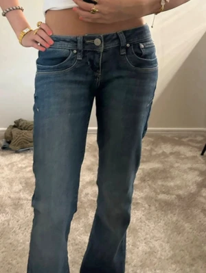 Blå bootcut jeans med låg midja - Säljer ett par blå bootcut jeans med låg midja och klassisk femficksdesign. Jeansen har en lätt tvättad look och raka ben som går ut lite nedtill. Perfekta för en avslappnad och trendig stil. Materialet är denim i bomull.