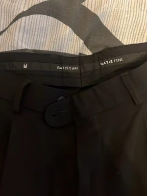 Svarta kostym  från Batistini - Snygga svarta kostymbyxor från Batistini med Kavaj klassisk rak passform och pressveck. Byxorna har bälteshällor, sidofickor och stängs med knapp och dragkedja. Perfekta för en stilren look.