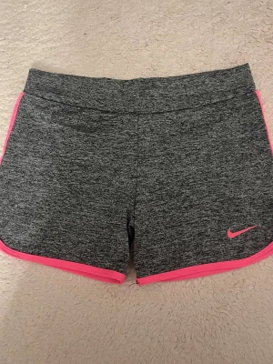 Grå träningsshorts från Nike - Snygga grå träningsshorts från Nike med rosa detaljer och logga. De har en sportig look och är perfekta för gymmet. Storlek S, aldrig använda🩷