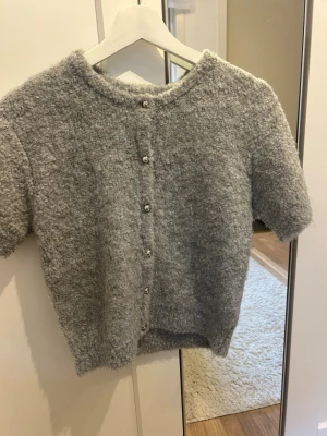 Grå kortärmad kofta med knappar - Mysig grå kofta från Gina tricot i fluffigt material med korta ärmar och rund hals. Koftan har dekorativa knappar framtill och en avslappnad passform💕