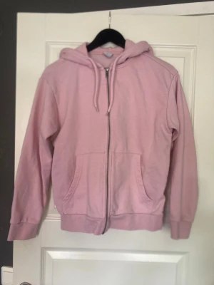 Ljusrosa hoodie med dragkedja - Ljusrosa hoodie från 157 med dragkedja framtill, två fickor och justerbar huva med snören. Tillverkad i mjukt och fleeceliknande material på insidan för extra komfort. Perfekt för en avslappnad och chill stil.