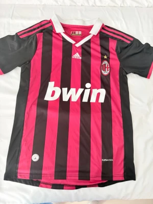AC Milan Ronaldinho matchtröja - Säljer en klassisk AC Milan fotbollströja från Adidas med Ronaldinho och nummer 80 på ryggen. Tröjan har röda och svarta vertikala ränder, klubbmärke på bröstet, Bwin som sponsor och Climacool-material för bra ventilation. Perfekt för fans och samlare!