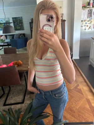 Halter topp linne - Säljer en söt ärmlös linnetopp med smala axelband och v-ringning. Toppen har ett randigt mönster i ljusa pastellfärger som mintgrön, rosa, gul och vit. Materialet känns mjukt och stretchigt, troligen bomull eller syntet. Perfekt för varma dagar och somriga outfits.