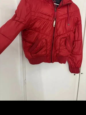Röd pufferjacka från edc by Esprit - Snygg röd pufferjacka från edc by Esprit med dragkedja framtill, två stora fickor och ribbade muddar vid ärmslut och midja. Jackan har en sportig look och är fodrad för extra värme. Perfekt för kalla vinterdagar. Jackan är i storlek L men jag skulle säga att den passar för M också.