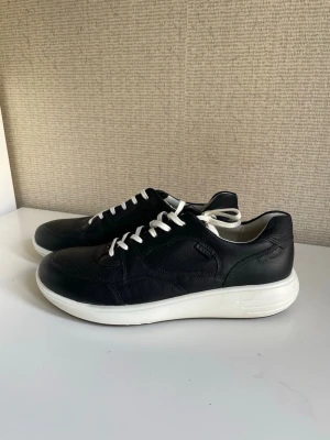 Ecco runner Svarta sneakers med vit sula, läder stl 42 oanvända  - Stilrena svarta sneakers med vit, tjock sula och vita snören. Skorna har en låg profil och är tillverkade i slätt läder med diskreta sömmar för en clean look. Perfekta för dig som gillar enkel och modern stil. Ecco, äkta skinn, stl 42, oanvända 