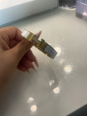 Vitt och guldigt armband med H-detalj - Snyggt armband i vitt och guld med en tydlig H-detalj framtill. 