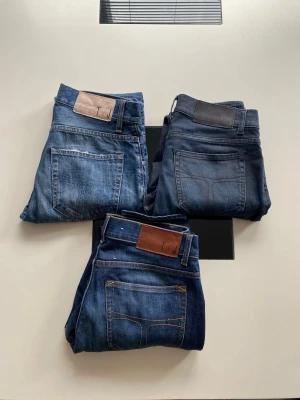Tre par blå jeans i olika tvättar - Säljer tre par klassiska blå jeans i olika tvättar, från ljusblå till mörkblå. Alla har fem fickor, raka ben och detaljer som kontrastsömmar och läderpatch bak i midjan. Perfekta för dig som vill ha ett par snygga och tidlösa jeans i garderoben.