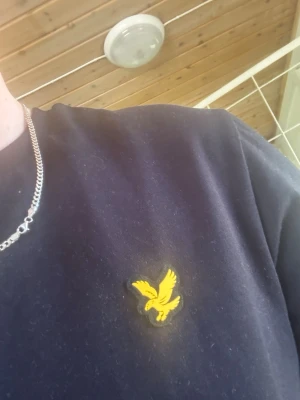 Svart t-shirt lyle and scott - Snygg svart t-shirt med en gul broderad logga på bröstet. Klassisk passform och korta ärmar, perfekt till jeans eller shorts. Tillverkad i mjukt bomullsmaterial för skön känsla hela dagen. Helt ny använd 1 gång för att ta bilder 