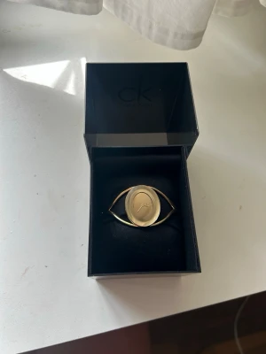 Guldfärgad klocka från Calvin Klein - Säljer en unik guldfärgad klocka från Calvin Klein med oval urtavla och stilren design. Klockan har ett öppet armband i metall som ger ett modernt och elegant intryck. Perfekt accessoar för dig som gillar minimalistisk stil.
