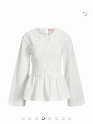 Vit blus med smock (aldrig använd) - Säljer en söt vit blus från JJXX med smockad överdel och lång ärm. Blusen har en lätt rynkad nederdel och är gjord i ett tunt, strukturerat tyg som känns luftigt och bekvämt. Perfekt att styla med jeans eller kjol för en trendig look.