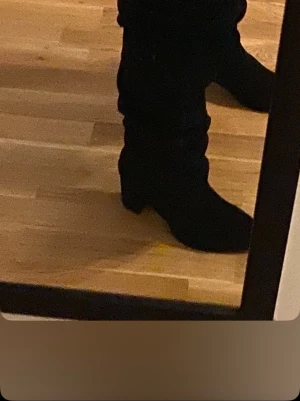 Svarta cowboy boots i mocka - Säljer ett par svarta cowboy boots med klassisk spetsig tå och låg klack. Bootsens material ser ut att vara mocka vilket ger en snygg och trendig look. Perfekta för dig som vill ha en western vibe i din outfit.