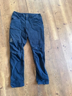 Svarta cargobyxor från Haglöfs - Snygga svarta cargobyxor från Haglöfs med flera praktiska fickor och dragkedja. Tillverkade i slitstarkt material som passar perfekt för äventyr och vardag. Klassisk passform och diskret Haglöfs-logga på benet.