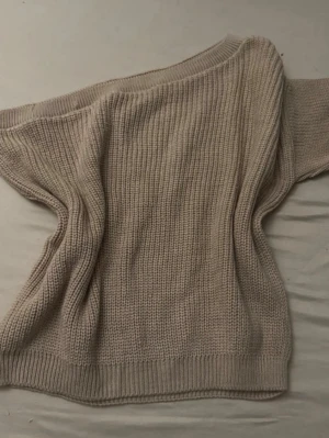 Beige oversized stickad tröja - Mysig beige stickad tröja i oversized modell med breda ärmar och ribbade muddar. Tröjan har en enkel, klassisk design och är gjord i ett tjockare garn som ger en avslappnad look. Perfekt för lager på lager och chill dagar.