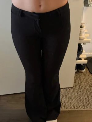 Svarta kostymbyxor med bootcut - Säljer ett par svarta kostymbyxor med bootcut-modell och hällor för skärp. Byxorna har en klassisk look med fuskfickor bak och är tillverkade i ett mjukt, stretchigt tyg som sitter snyggt. Perfekta för en clean och stilren outfit.