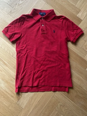 Piké Polo Ralph Lauren  - Klassisk röd pikétröja från Polo Ralph Lauren med korta ärmar och krage säljes. Pikén är i storlek 8 år och i mycket fint skick. 