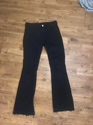 Svarta bootcut jeans med rå kant - Säljer ett par svarta bootcut jeans med rå, fransad kant nertill. Jeansen har låg midja, fickorna framtill är bara design, alltså ej fickor. Jeansen är lite korta på mig som är 168. Skulle säga att materialet känns som en blandning av jeans och kostymbyxor.