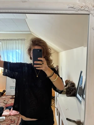 Svart transparent loose t-shirt med mörkare glitter-detaljer - Säljer en svart transparent t-shirt med loose passform och korta ärmar. T-shirten har ett diskret mönster i tyget och är perfekt för dig som gillar en avslappnad och trendig stil. Materialet känns lätt och luftigt.