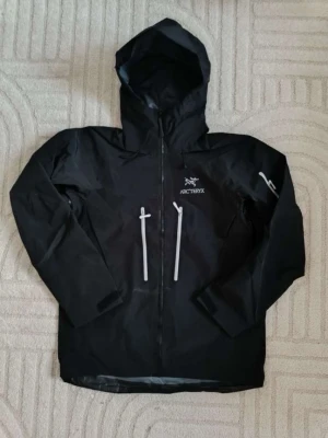 Svart regnjacka från Arc'teryx - Arc’teryx Alpha SV jacka i svart, storlek L.  Jackan är i mycket fint skick och har använts väldigt lite. Inga större skador eller märken vad jag kan se. Säljer den eftersom den inte används längre.  • Modell: Alpha SV • Färg: Svart/Orca • Storlek: L • Skick: Mycket fint skick • Säljs eftersom den inte används  📍 Endast möte i Märsta 💵 Betalning vid möte 🤝 Seriösa köpare är välkomna att komma och kolla på jackan innan köp. Observera gärna jackan (vet ej om den är äkta, köpt från Vinted)