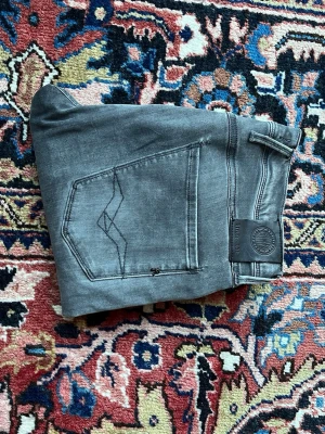 Replay anbass  - Säljer dessa snygga grå/svarta slim-jeans i storlek 30/32. Cool, urtvättad grå finish med diskreta slitningar och små svarta stänk/fläckar som ger en rå och streetig look. Jeansen sitter tight och följsamt över benen – se bilderna för passform. Jag är 175 cm lång och väger 70 kg, så du får en bra bild av hur de sitter på mig. Skick: Använda men i fint skick. Storlek: 30/32 Hör av dig om du vill ha fler bilder eller har frågor!