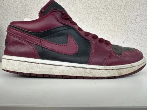 Air Jordans 1 Low - Snygga Air Jordan 1 Low sneakers i svart och vinrött läder med klassisk vinge-logga på hälen och matchande vinröda skosnören. Ikonisk Nike Swoosh på sidan och svart Jumpman på plösen. Perfekta för dig som gillar streetwear och vill sticka ut. Bra pris!