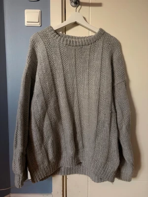 Grå oversized stickad tröja - Mysig grå stickad tröja med bred ribbad rund halsringning och avslappnad passform. Tröjan har långa ärmar och ribbade muddar vid ärmslut och nederkant. Perfekt nu när det börjar bli kallt igen