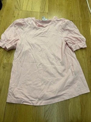 Ljusrosa topp från Vero Moda - Supersöt ljusrosa topp från Vero Moda med puffiga korta ärmar och rund halsringning. Tillverkad i mjuk bomull som känns skön mot huden. Perfekt för dig som gillar en enkel men ändå trendig stil.