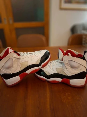 Vita och röda höga jordans - Snygga höga sneakers i vitt, rött och svart med cool design och tydliga detaljer. Skorna har en kraftig sula med röd och svart färg, samt vita partier på ovandelen. Perfekta för dig som vill sticka ut med din stil.