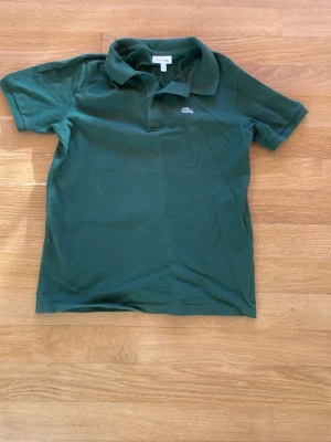 Lacoste piké  - Klassisk mörkgrön pikétröja med krage och korta ärmar. Tröjan har en liten broderad logga på bröstet och är tillverkad i mjuk bomull. Perfekt till en avslappnad och stilren look.