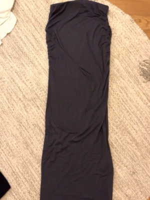 Mörkgrå långkjol - En enkel och stilren mörkgrå långkjol. Kjolen har en rak passform och lätt rynkade detaljer på sidan för en snygg siluett. Perfekt att matcha med en crop top eller oversized tröja.