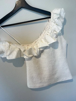 Vit oneshoulder topp med volang - Säljer en superfin vit oneshoulder topp med volang från Zara. Helt ny med prislapp kvar. Storlek s. 