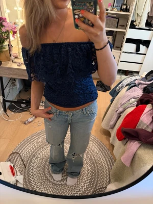 Mörkblå offshoulder spetsblus - Säljer en mörkblå offshoulder blus i spets med croppad passform. Toppen har fina spetsdetaljer och är axelbandslös vilket ger en trendig look. Perfekt att styla med jeans eller kjol för en cool outfit.