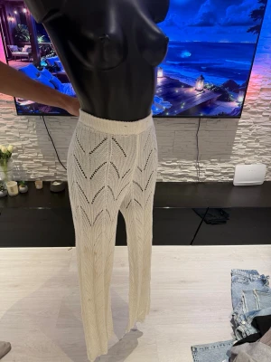 Vita virkade leggings med mönster - Säljer ett par vita virkade leggings med snyggt hålmönster och hög midja. De har raka ben och är genombrutna vilket ger en trendig och luftig look. Perfekta att styla över bikinin eller med en oversized skjorta för en chill vibe.