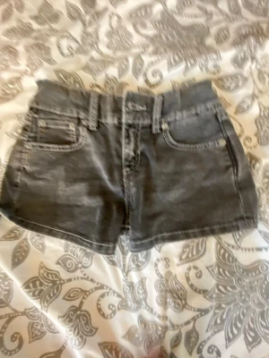 Grå denimshorts med fickor - Snygga grå denimshorts med klassisk femficksdesign, bälteshällor och knappstängning. Shortsen har dekorativa sömmar och bakfickor med lock och knapp. Perfekta för varma dagar och enkel att matcha med olika toppar.