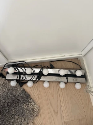 Sminkspegelbelysning med LED-lampor - Snygg sminkspegelbelysning med åtta runda LED-lampor på en silverfärgad metallist. Perfekt för att få riktigt bra ljus när du sminkar dig. Lamporna är vita och listen har en modern, stilren design som passar i de flesta rum. Kopplas in med sladd.