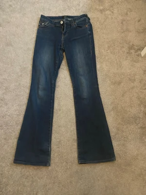 Mörkblå bootcut jeans med fickdetaljer - Snygga mörkblå bootcut jeans med klassisk femficksdesign och markerade sömmar. Baksidan har dekorativa fickor med lock och knappar. Jeansen har en lätt tvättad look och är tillverkade i denim med lite stretch för skön passform.