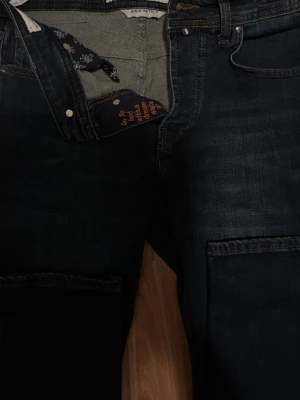 Mörkblå jeans från Jacob Cohën - Snygga mörkblå jeans från Jacob Cohën med klassisk femficksmodell och diskreta slitningar. Insidan har ett unikt mönstrat foder och broderad text. Jeansen har knappgylf och kontrastsömmar för en cool look.