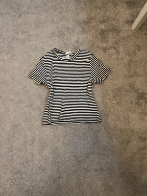 Randig svartvit t-shirt - Säljer en klassisk svartvit randig t-shirt med rund hals och korta ärmar. T-shirten har en normal passform och är tillverkad i mjuk bomull, perfekt för en avslappnad och stilren look.