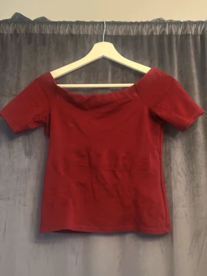 Röd offshoulder topp - Snygg röd offshoulder topp med korta ärmar och figurnära passform. Perfekt för dig som vill ha en enkel men stilren topp till din outfit. Tillverkad i mjukt material som känns skönt mot huden.