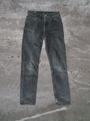 Levis 501 - Säljer ett par grå levis 501 med rak passform och klassisk femficksdesign. Jeansen har en snygg tvättad look och detaljer som metallknappar och nitar. Materialet är kraftig denim som ger en cool vintage vibe. Perfekta till sneakers eller boots. Bredden är 33 cm och längden är 99 cm