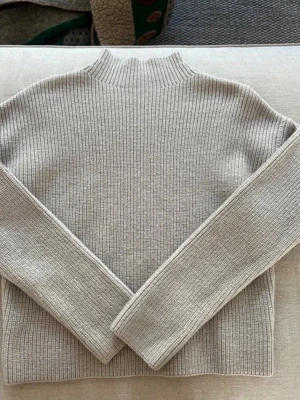 Ljusgrå ribbstickad tröja Filippa K - Säljer en stilren ljusgrå ribbstickad tröja från Filippa K. Tröjan har hög hals, raka ärmar. Väldigt fin och knappt använd! 