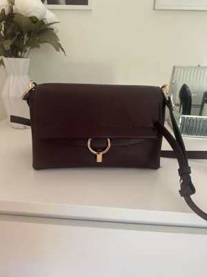 Mörkbrun axelväska i läderlook - Snygg mörkbrun axelväska.Perfekt för dig som gillar minimalistisk och elegant design