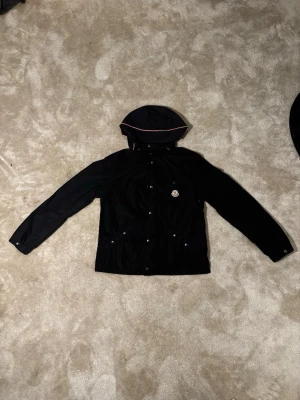 Svart regn jacka från Moncler - Snygg svart regnjacka från moncler. Jackan är i riktigt fint skick utan minsta skräma eller fläck. Den är storlek 164 men är stor i storleken så passar personer upp till nästan 170 cm. Priset är 2500 kr men kan diskuteras vid lätt affär. Jackan är 100% riktig!