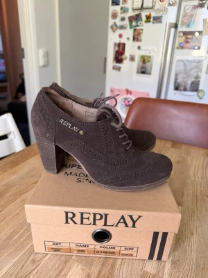 Bruna mocka pumps från Replay - Snygga bruna pumps från Replay i mjuk mocka med snörning framtill och dekorativa broguemönster. Skorna har en kraftig klack och rundad tå, vilket ger en cool och trendig look. Perfekta för dig som vill ha något unikt till din outfit.Använda bara vid ett tillfälle 